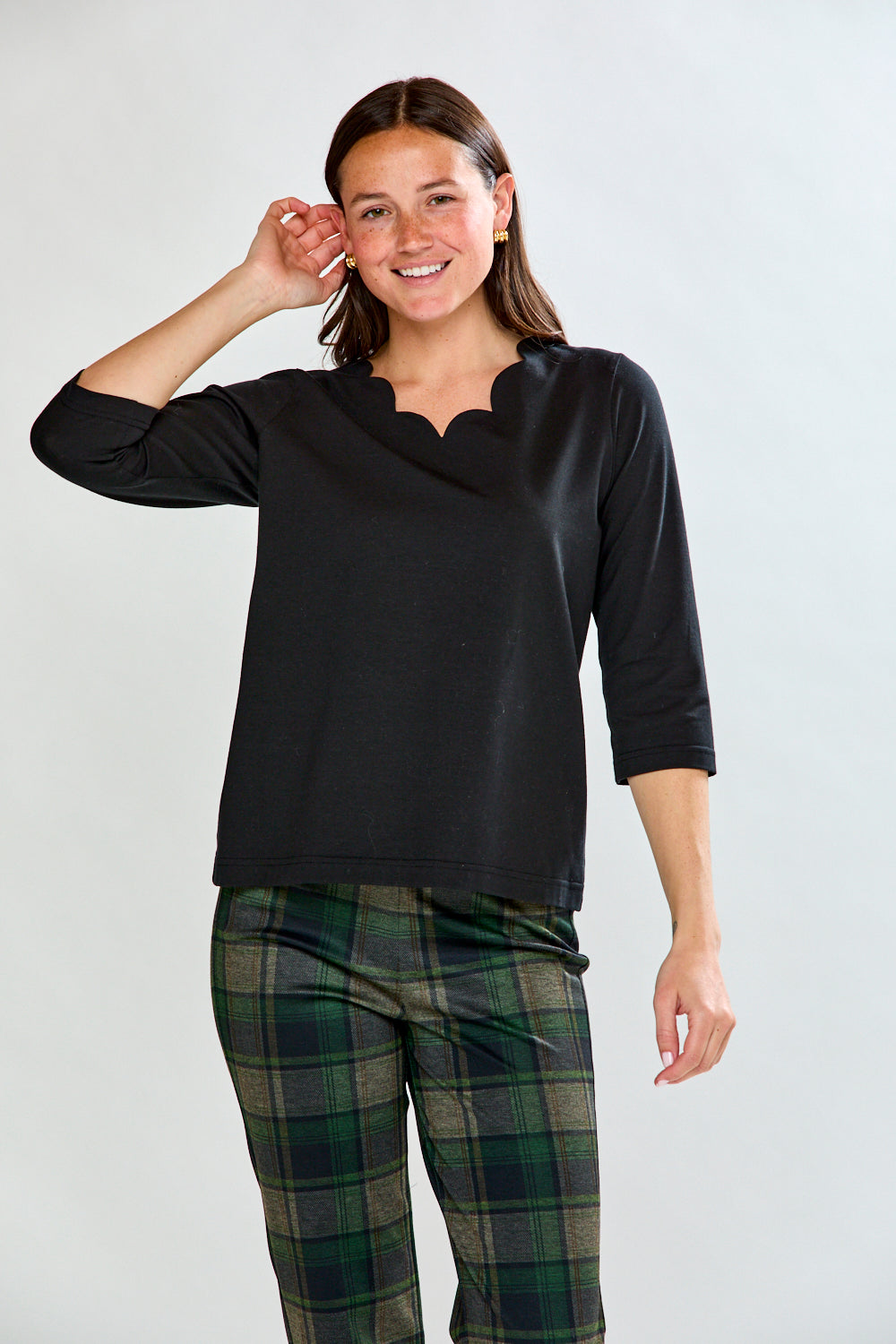 Woman wearing a black top with scalloped neckline and plaid pants on a white background