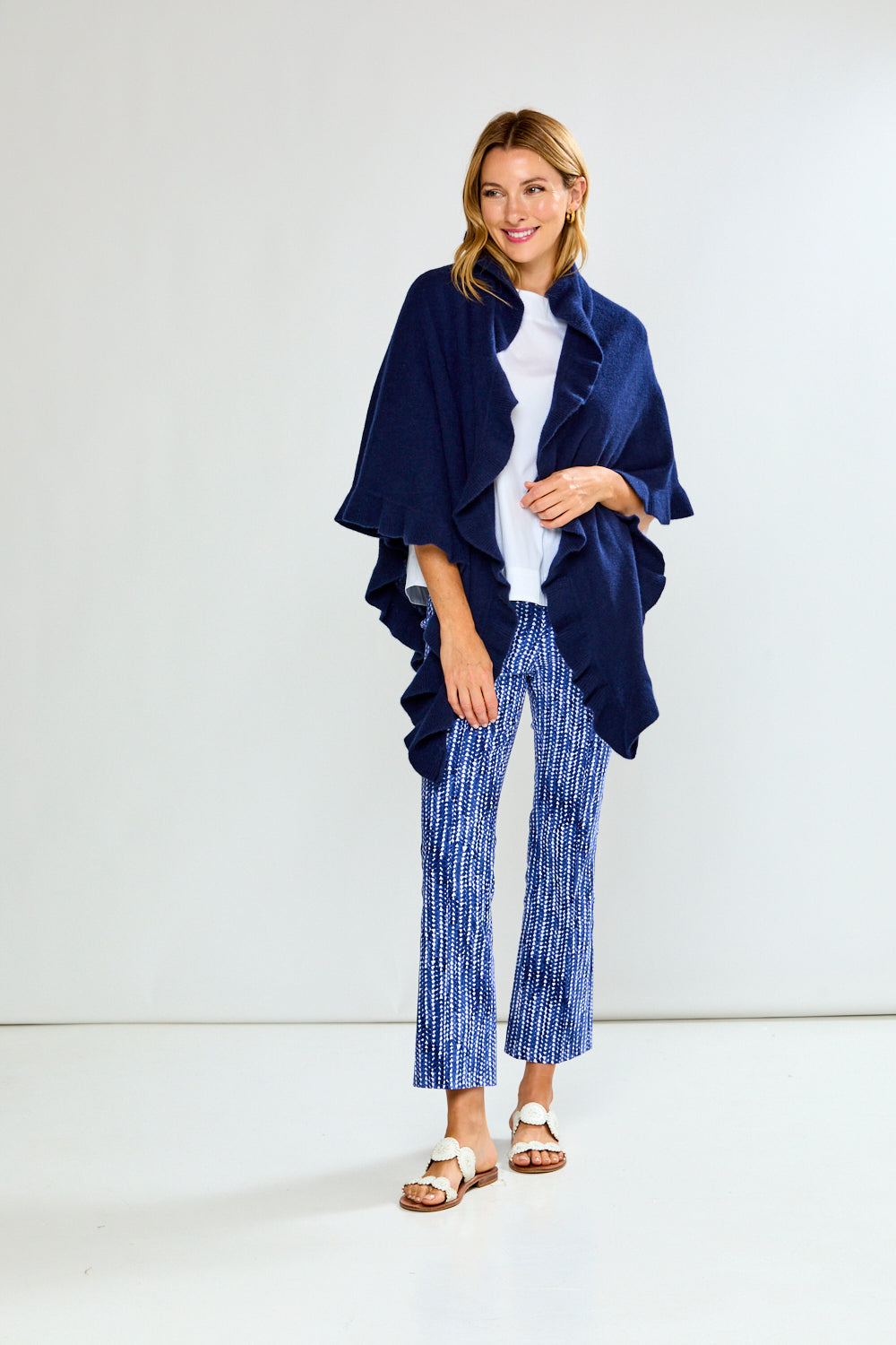 Woman wearing a navy blue ruffle triangle wrap over a white top and blue patterned pants on a white background