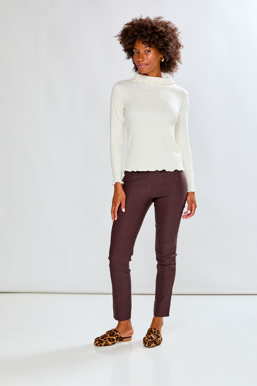 Woman wearing a white sweater and brown pants against a white background