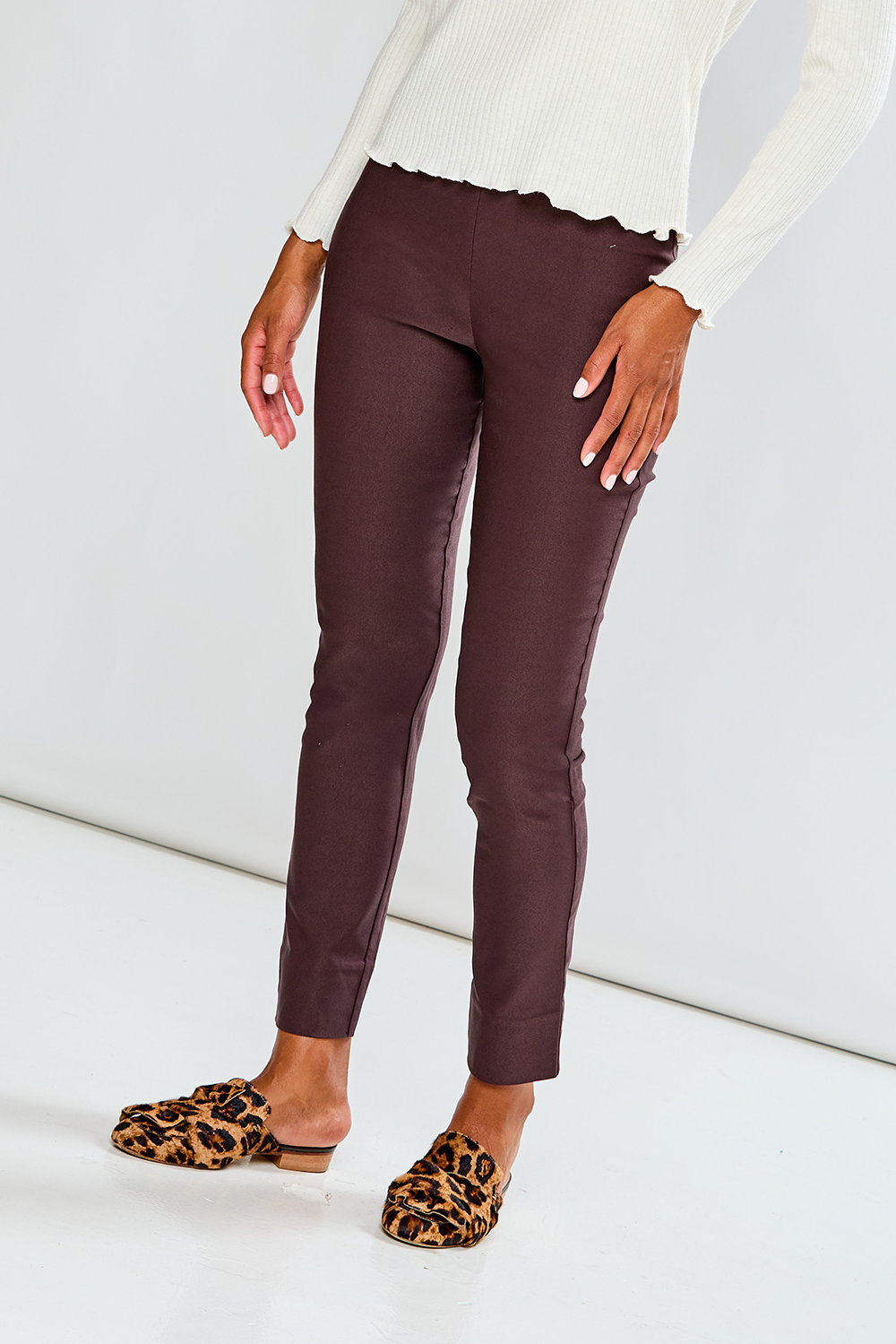 Person wearing brown pants with a white top and leopard print shoes on a light background