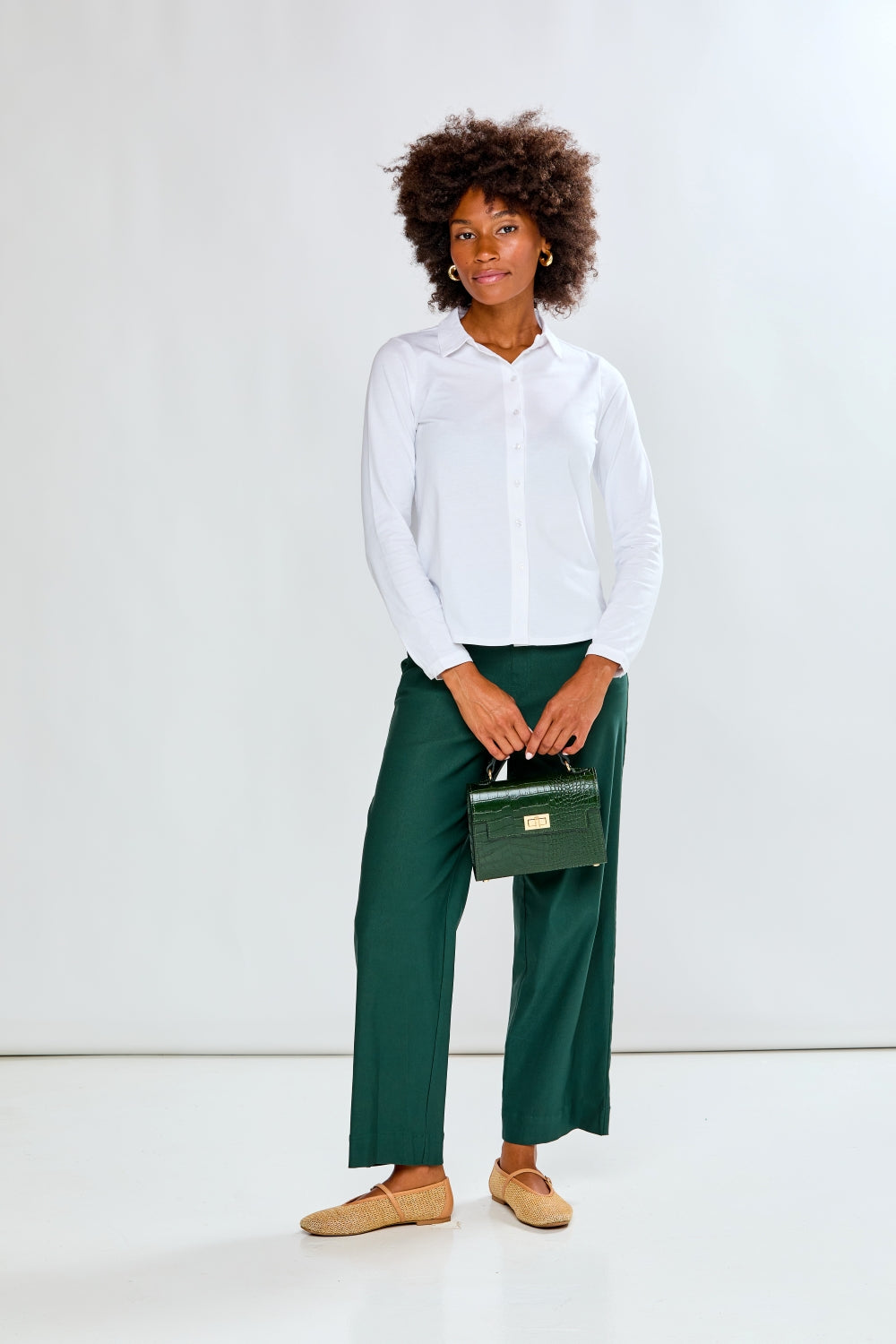 Person wearing a white shirt and green pants holding a green handbag against a white background