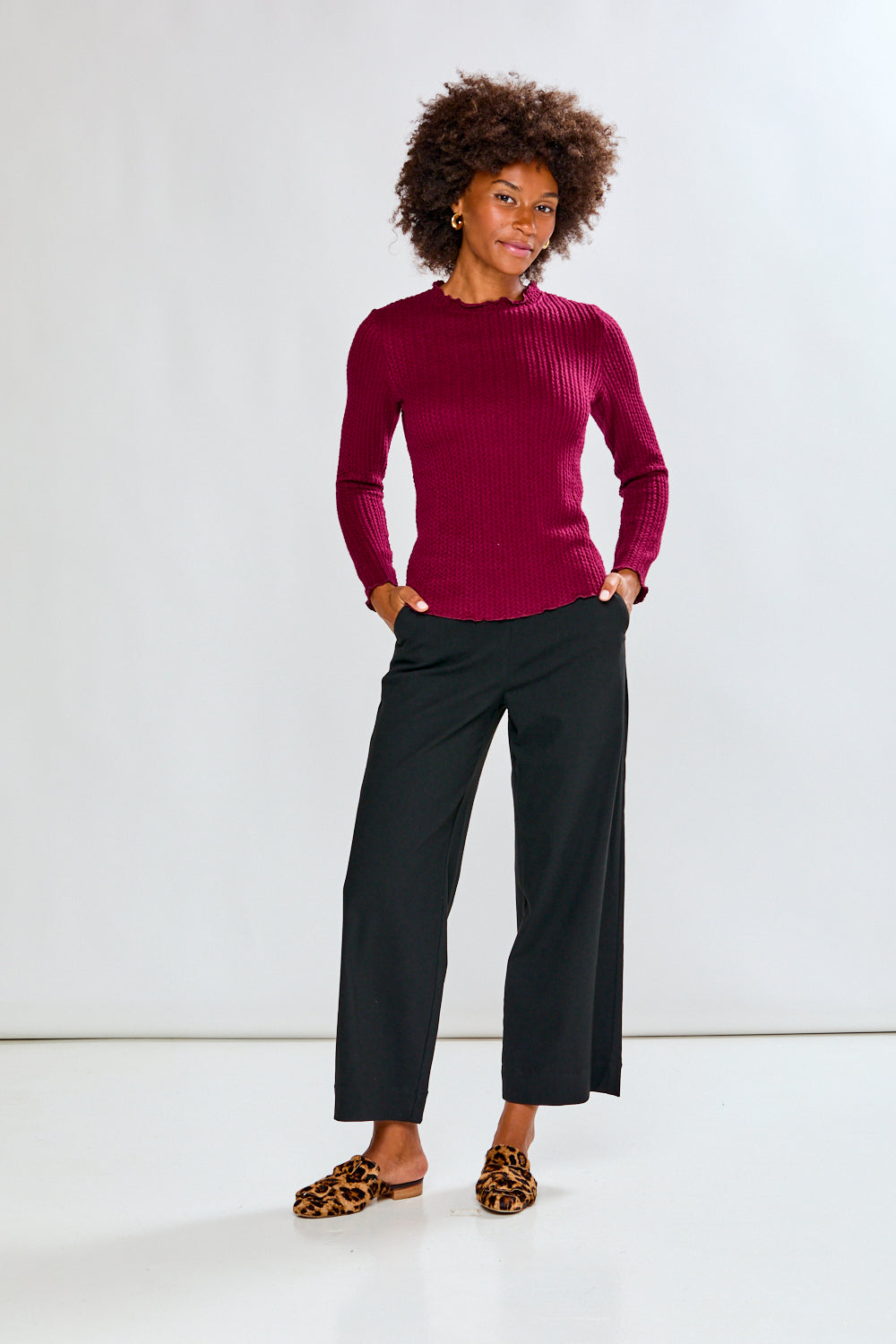 Woman wearing a purple sweater and black pants against a white background