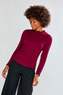 Woman wearing a burgundy sweater and black pants against a light gray background