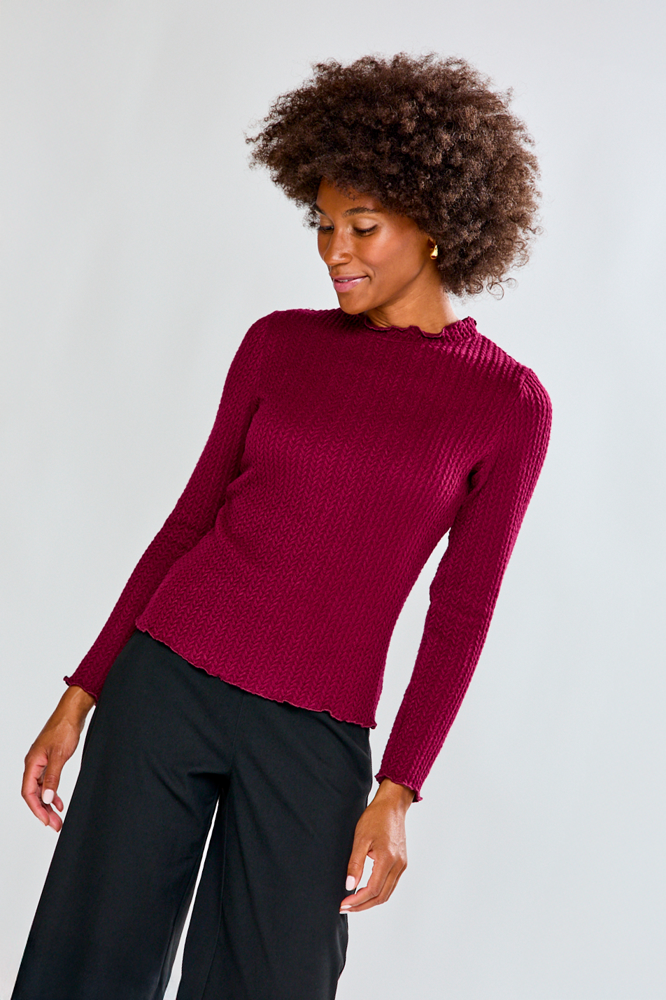 Woman wearing a burgundy sweater and black pants against a light gray background