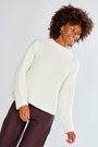 Woman wearing a cream sweater and brown pants against a white background