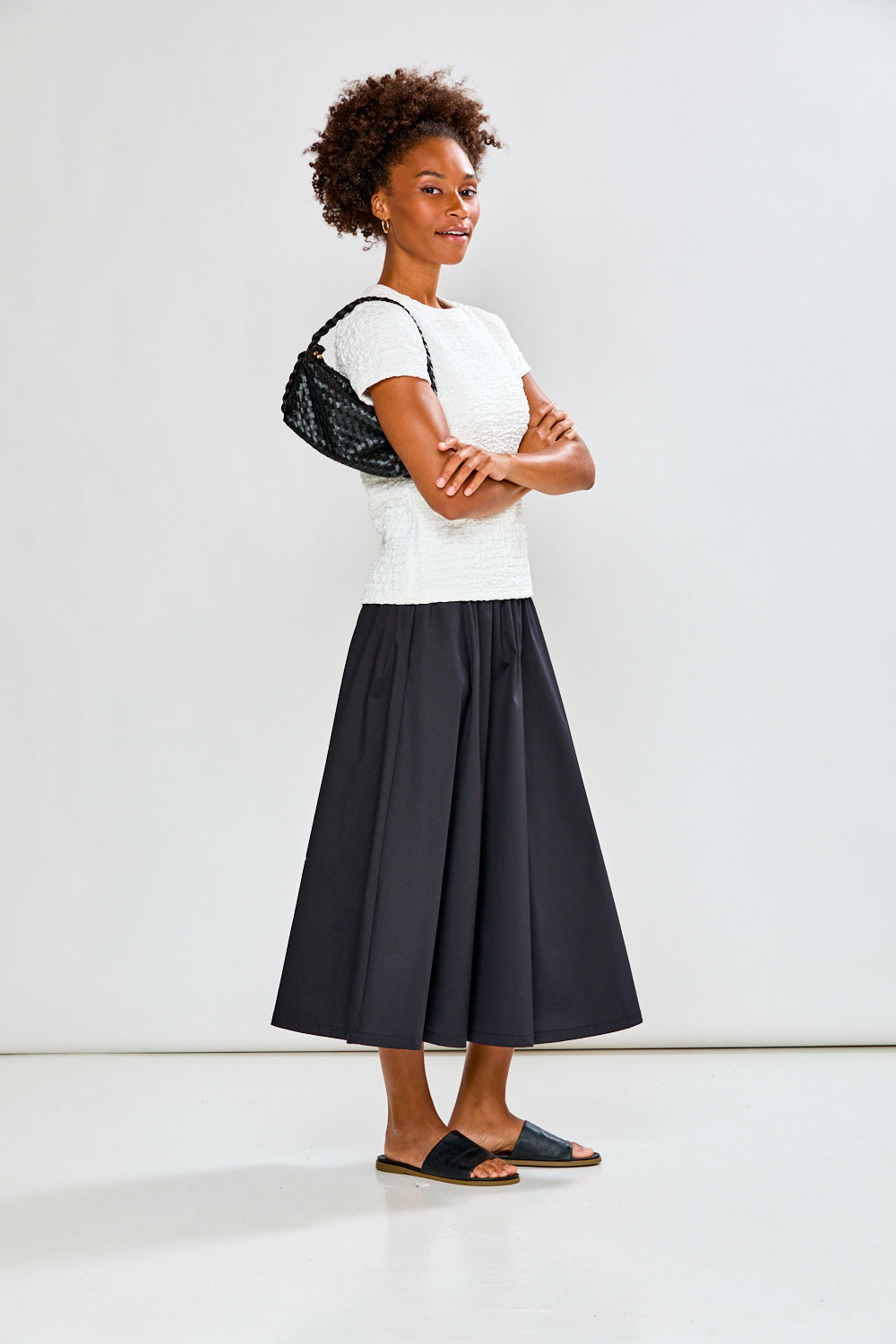 Woman wearing a white top and black skirt with a black bag against a white background