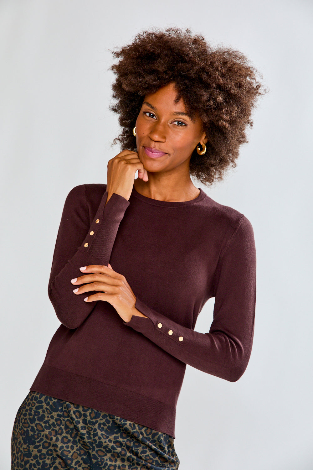 Woman wearing a maroon sweater with decorative buttons on a plain background