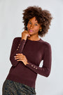 Woman wearing a maroon sweater with decorative buttons on a plain background