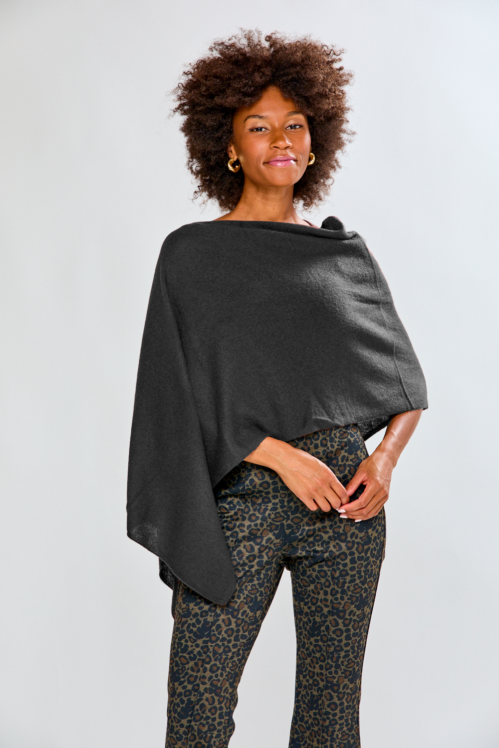 Woman wearing a dark gray poncho over a patterned outfit on a light background