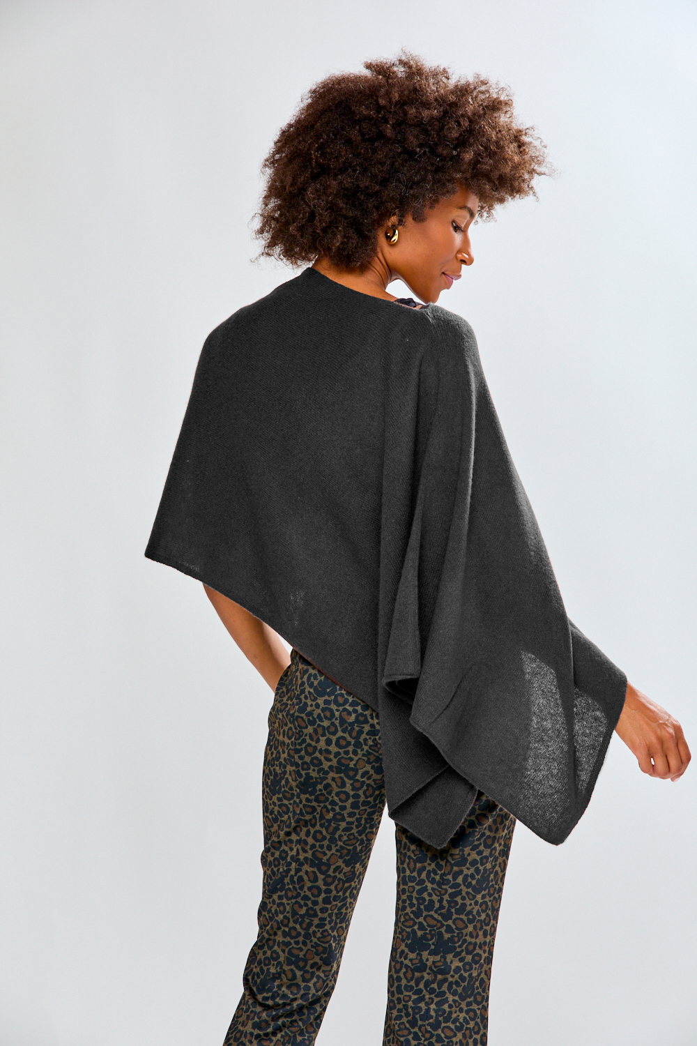 Person wearing a dark gray poncho over leopard print pants on a light gray background