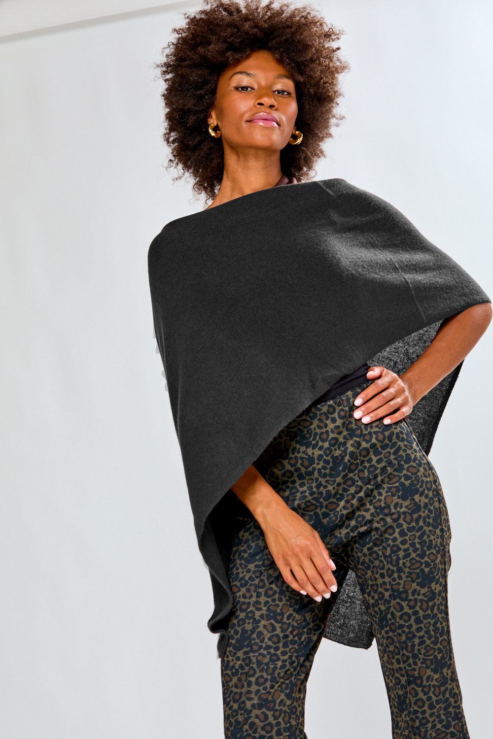 Woman wearing a dark gray poncho over a patterned outfit against a light background