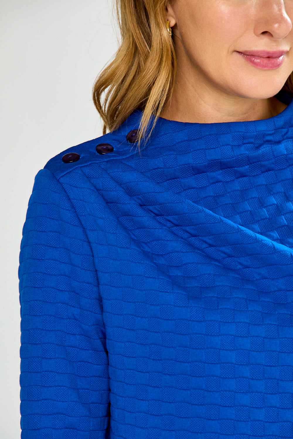 Close-up of a blue textured garment with buttons on a white background