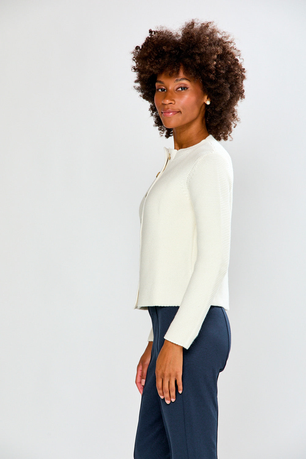 Woman wearing a white cardigan and navy pants against a plain background