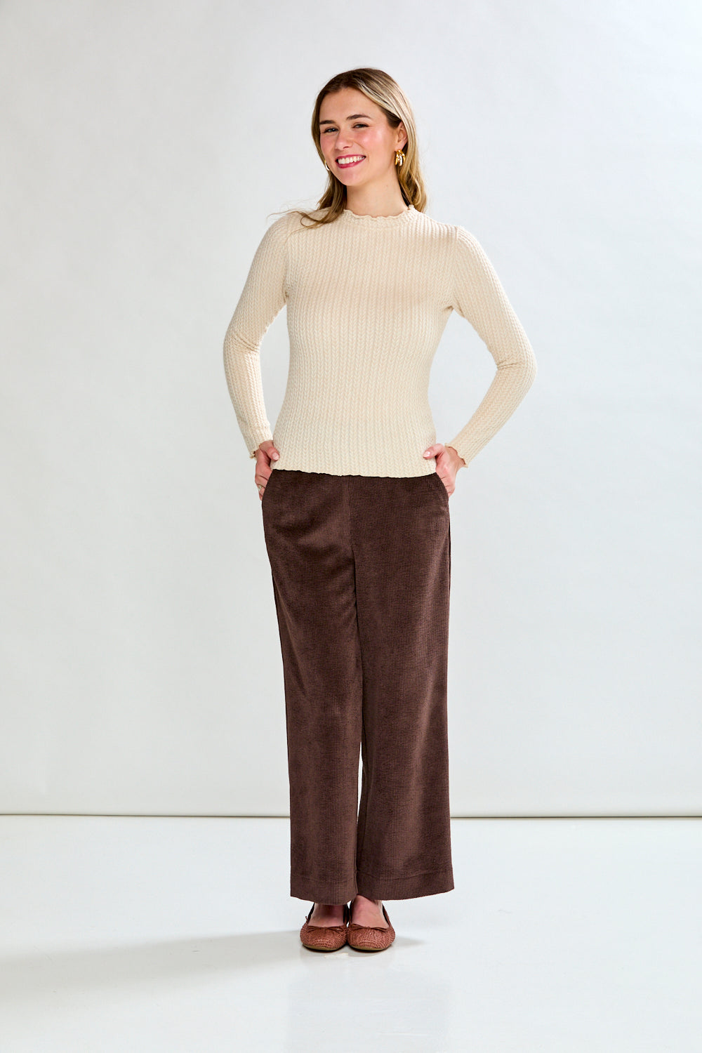 Woman wearing a beige ribbed shirt and brown pants against a white background