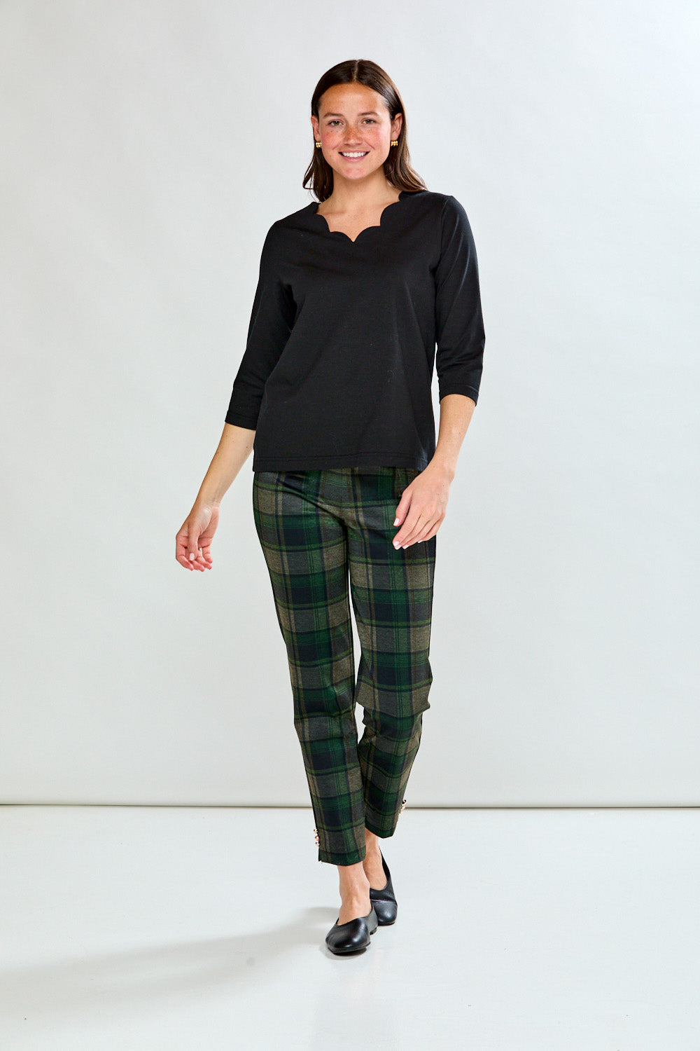 Woman wearing a black top and green plaid pants against a white background