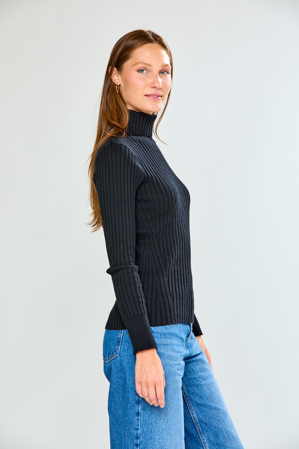 Woman wearing a black ribbed turtleneck sweater and blue jeans on a white background