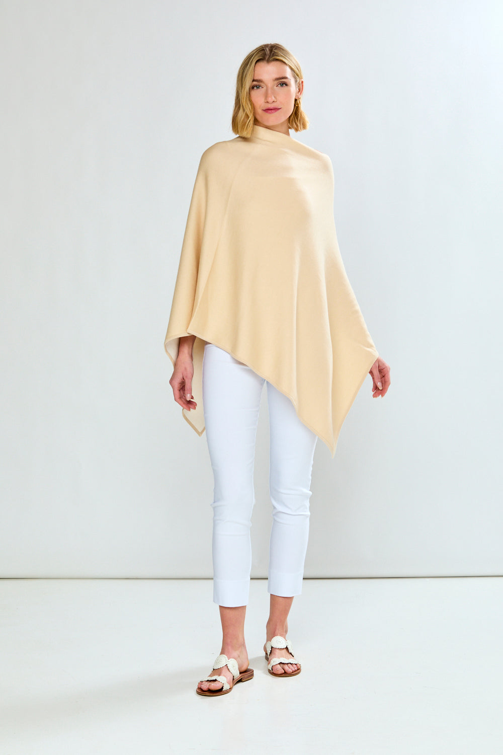 Woman wearing a beige poncho and white pants on a white background