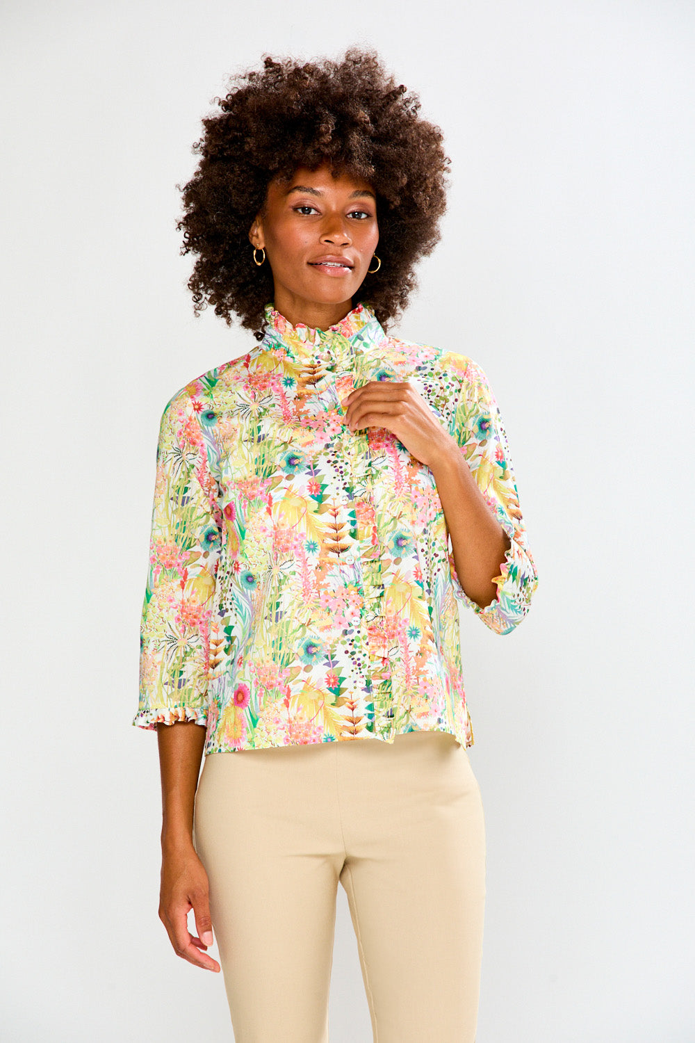 Woman wearing a floral blouse and beige pants against a white background