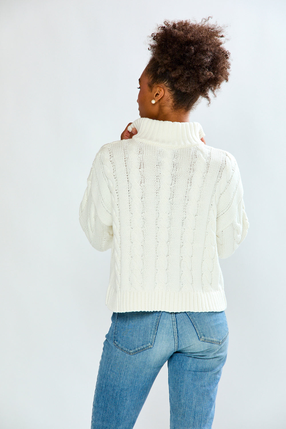 Person wearing a white cable knit sweater and blue jeans on a light gray background