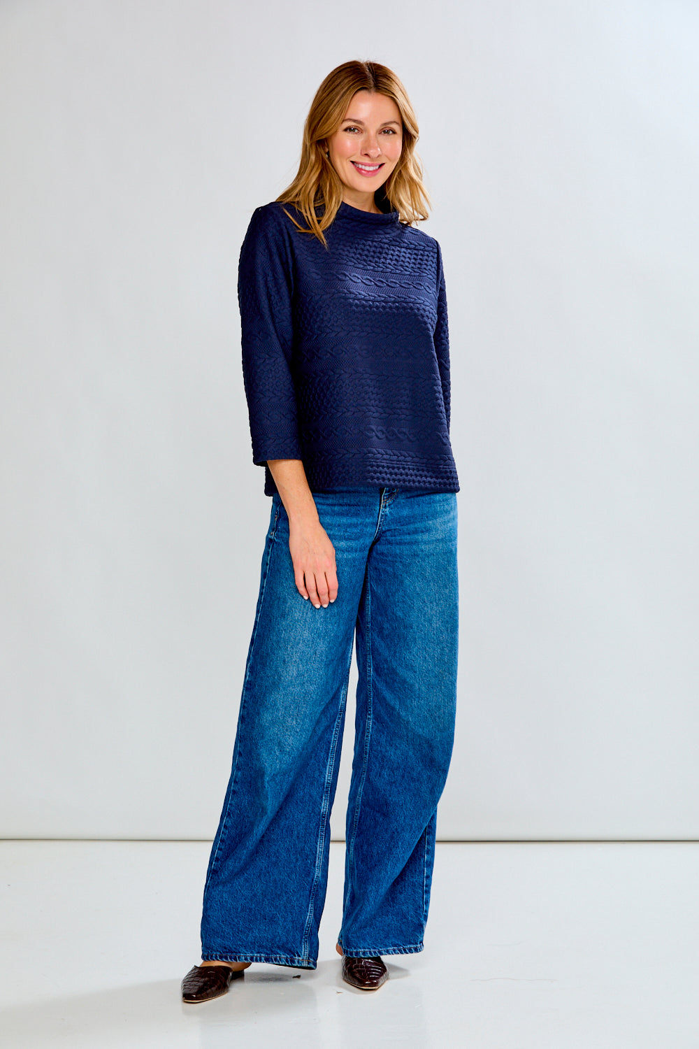 Woman wearing a navy blue textured sweater and blue jeans on a white background