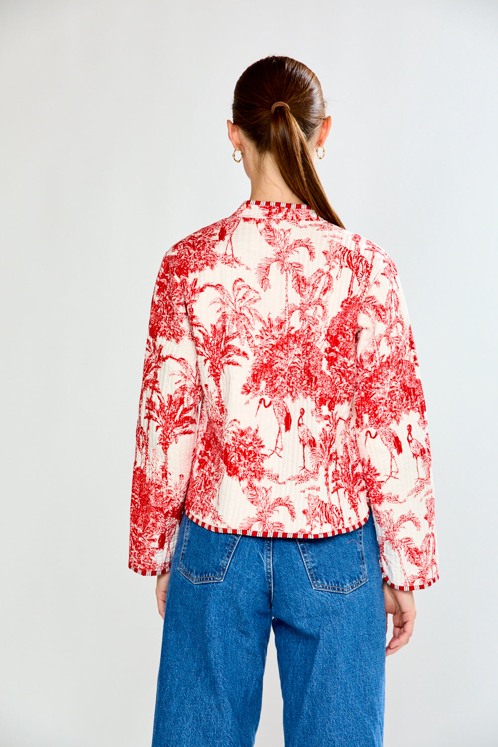 Person wearing a red and white patterned blouse with blue jeans on a plain background