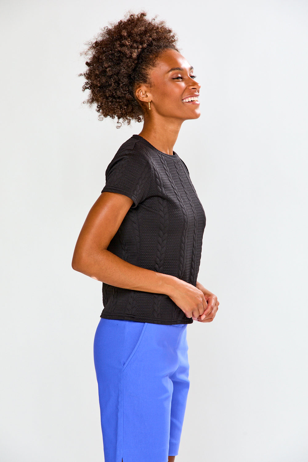 Woman wearing a black textured top and blue pants on a white background