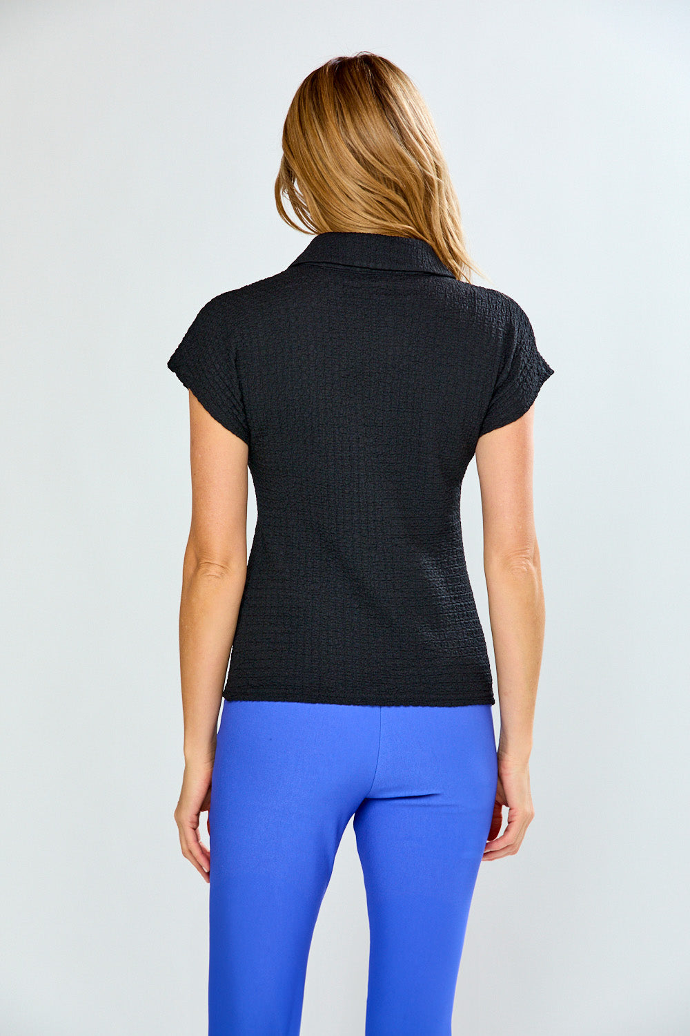 Woman wearing a black short-sleeve top and blue pants on a light gray background