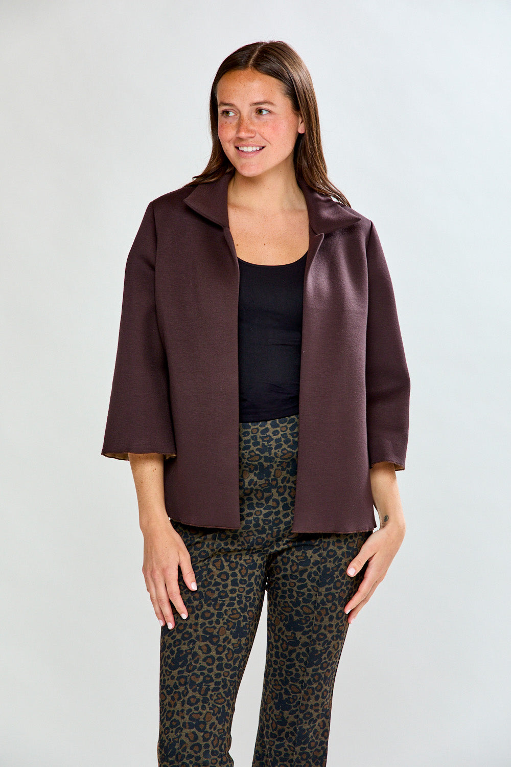 Woman wearing a brown jacket over a black top and patterned pants on a white background