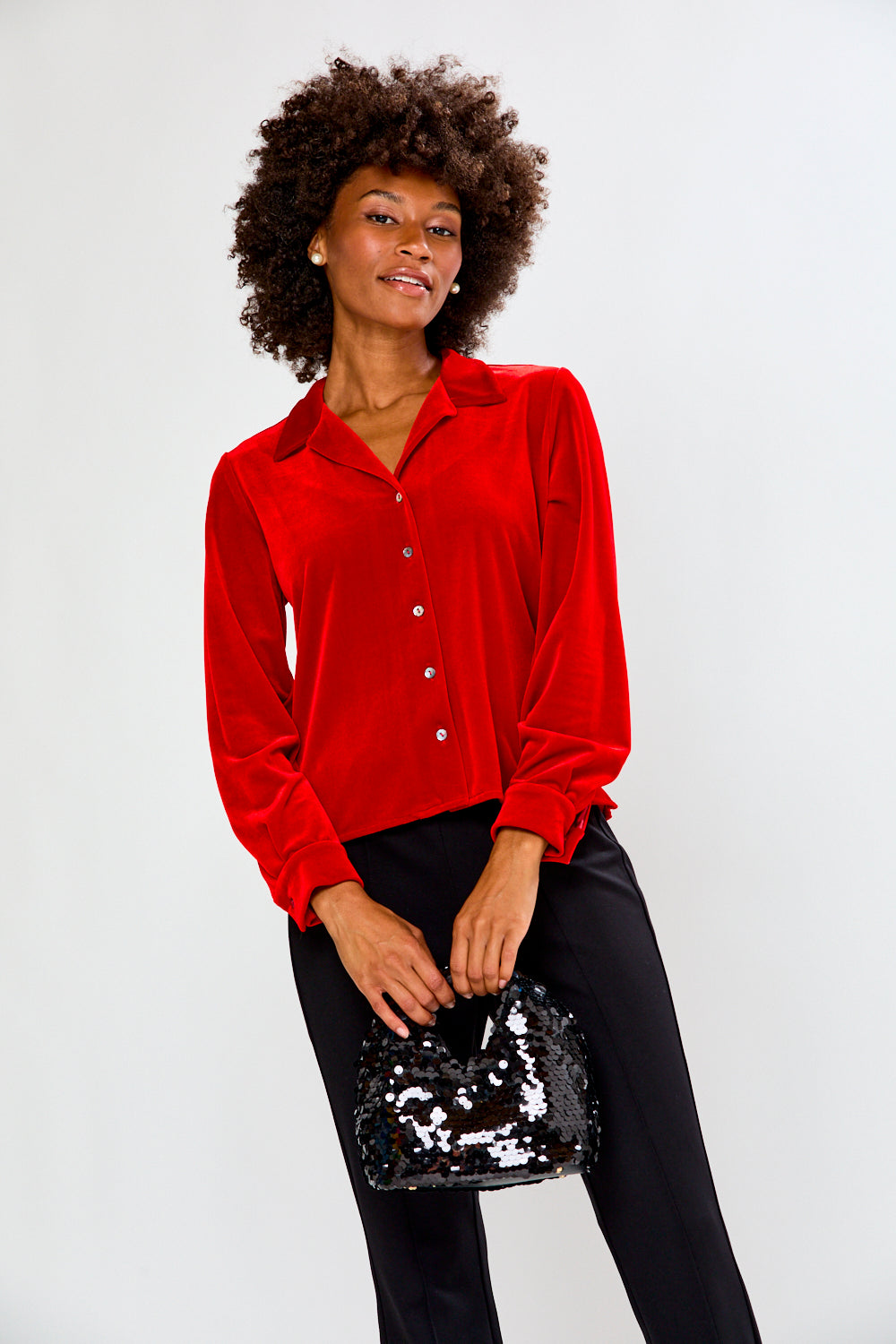 Woman wearing a red blouse and holding a black sequin handbag against a white background