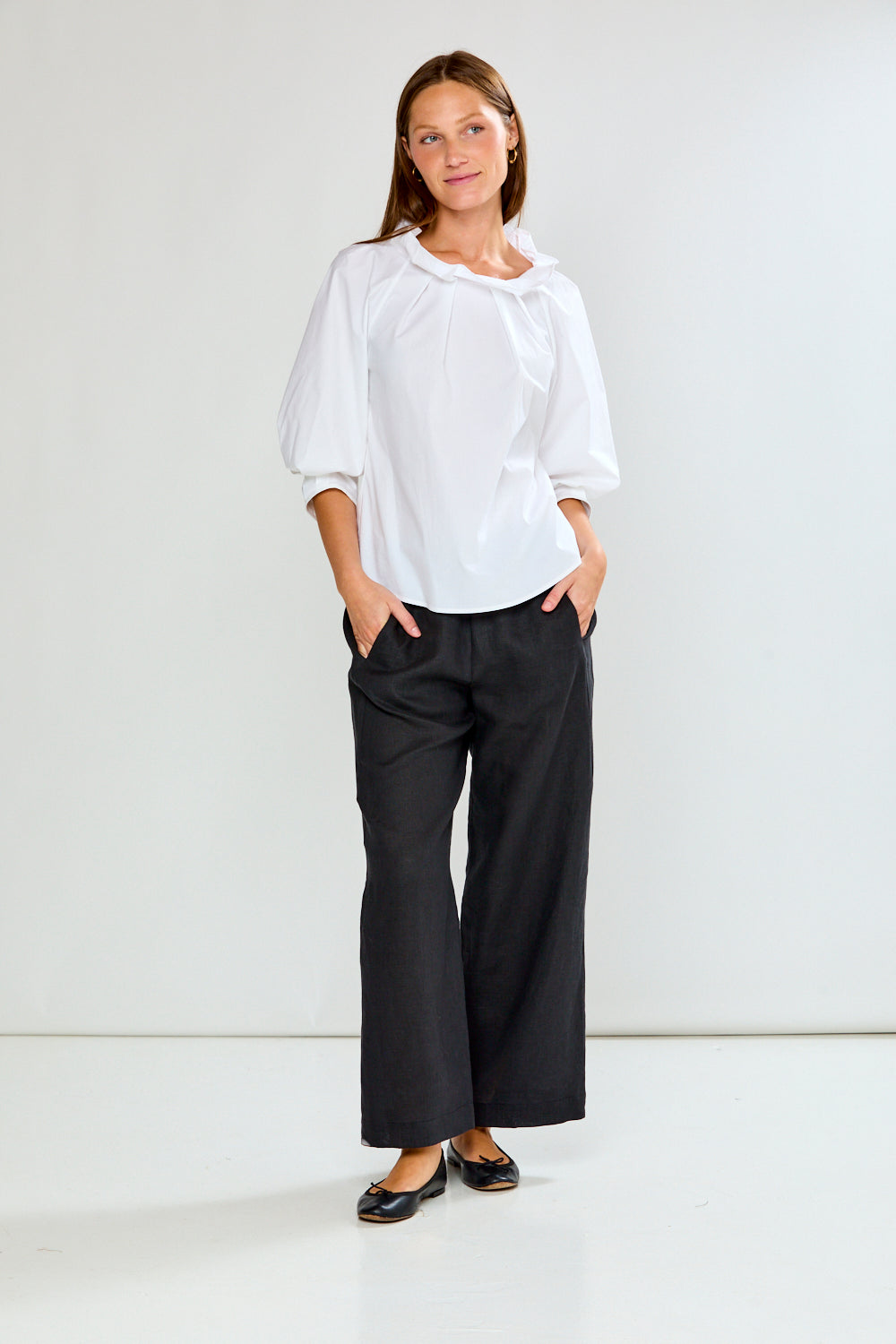 Woman wearing a white blouse and black pants against a white background