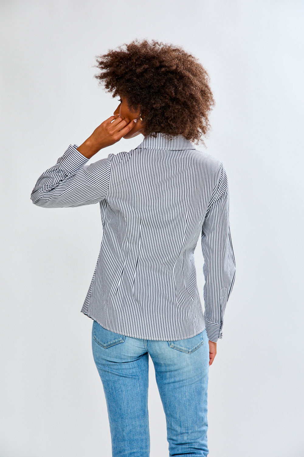 Woman wearing a striped shirt and jeans on a plain background