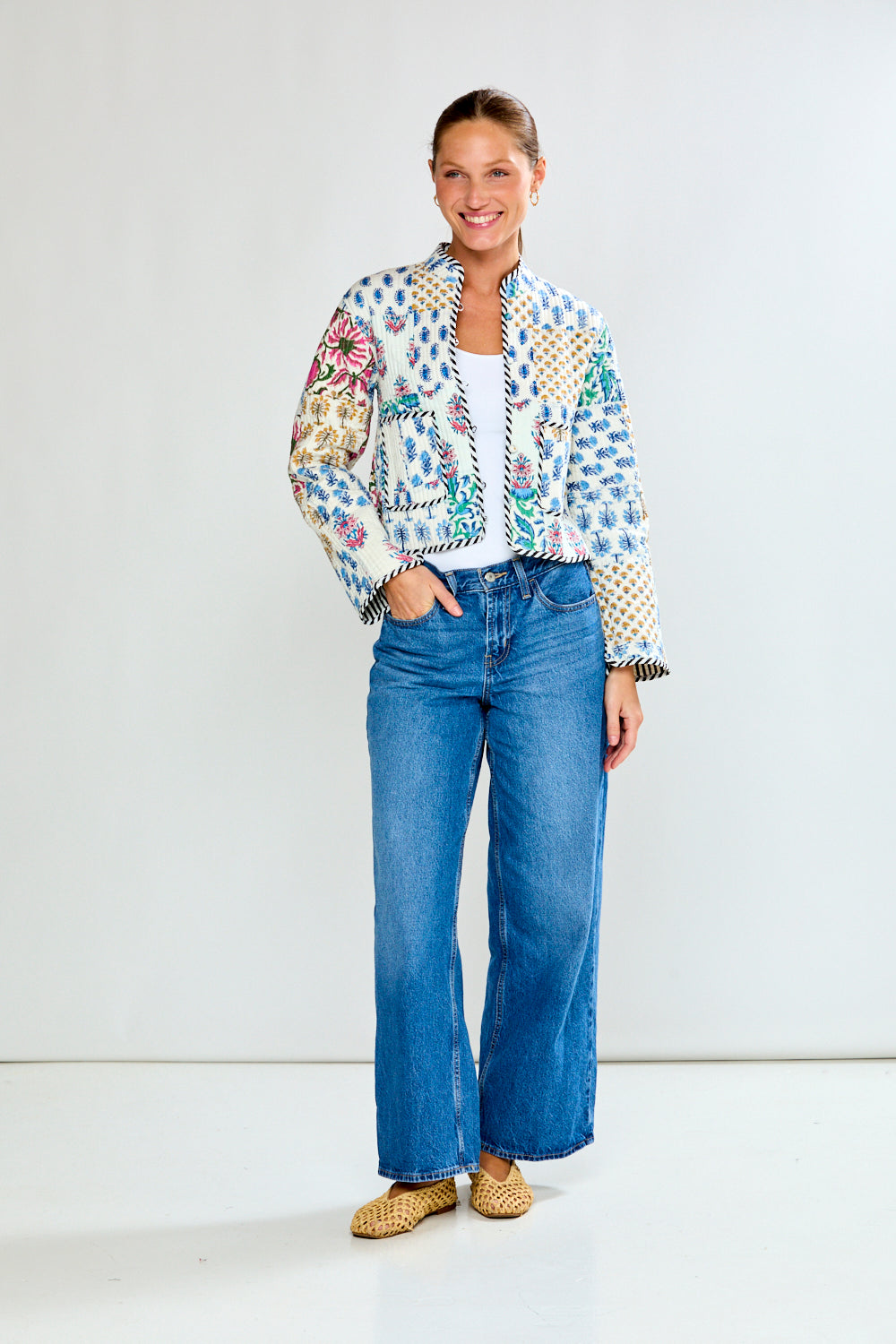 Woman wearing a colorful jacket and blue jeans on a white background