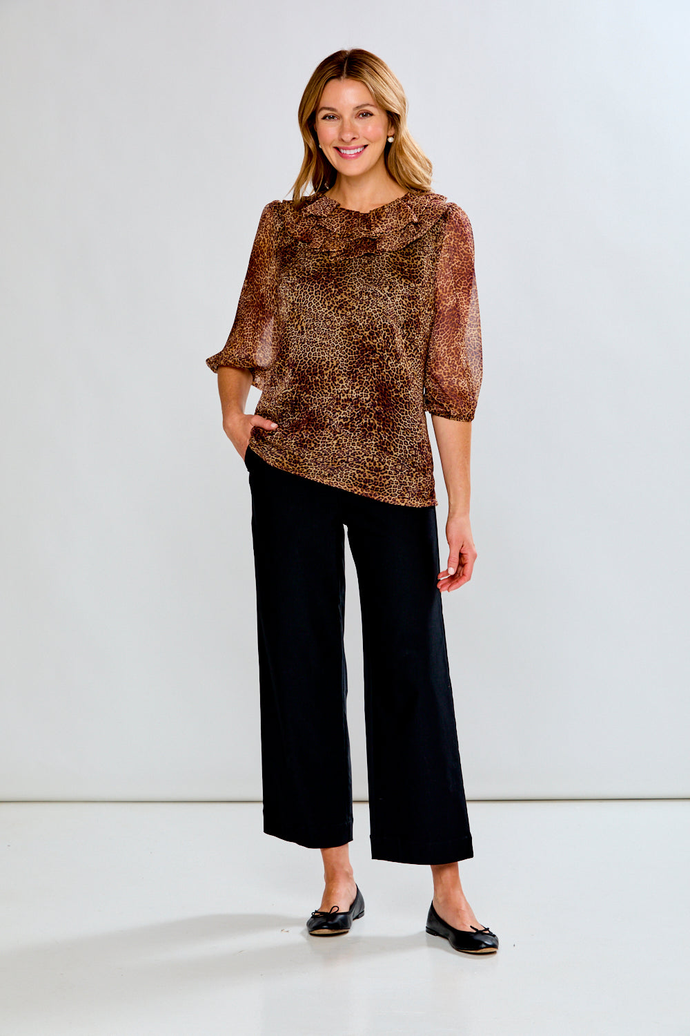 Woman wearing a patterned top and black pants against a white background