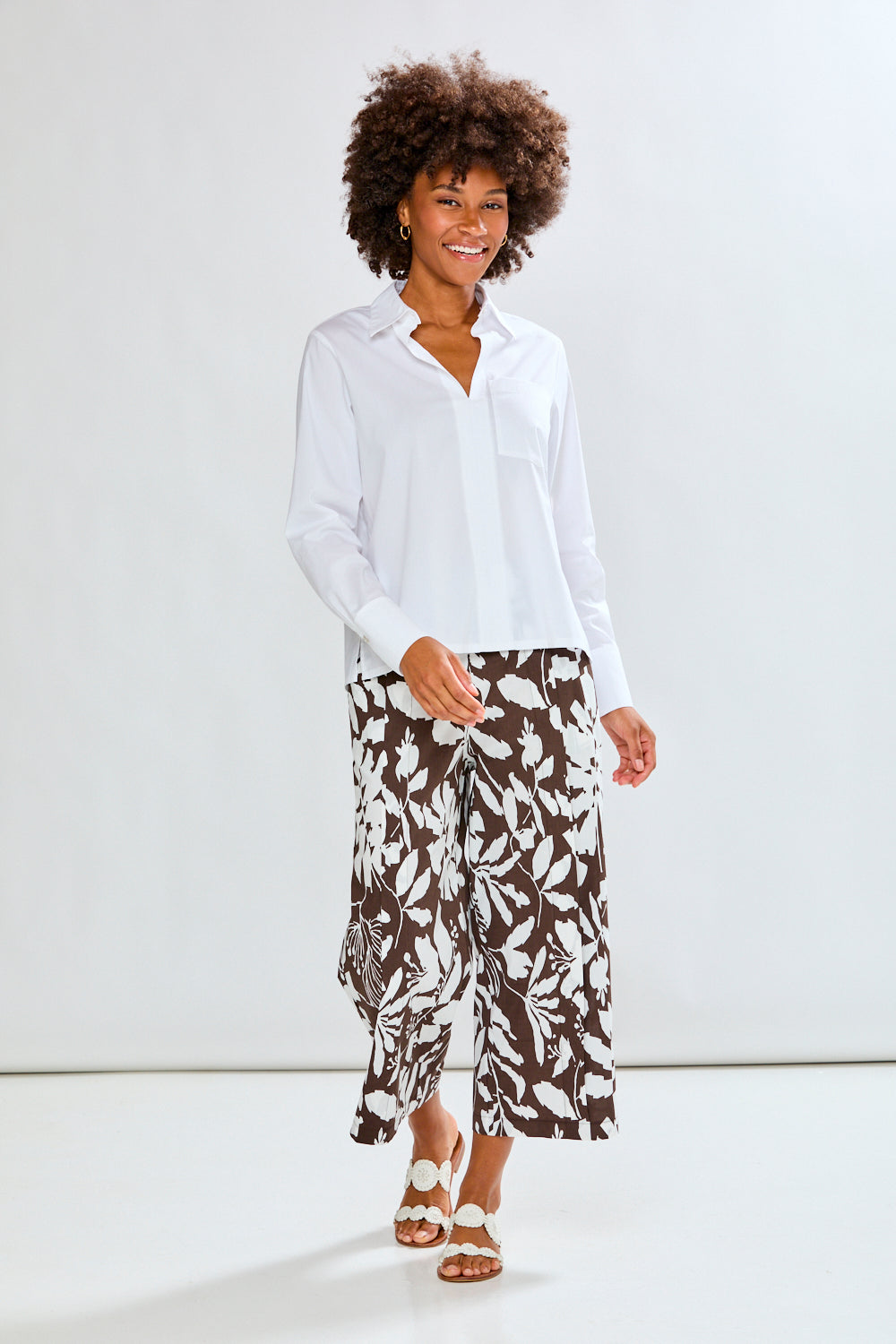 Woman wearing a white blouse and patterned pants against a plain background