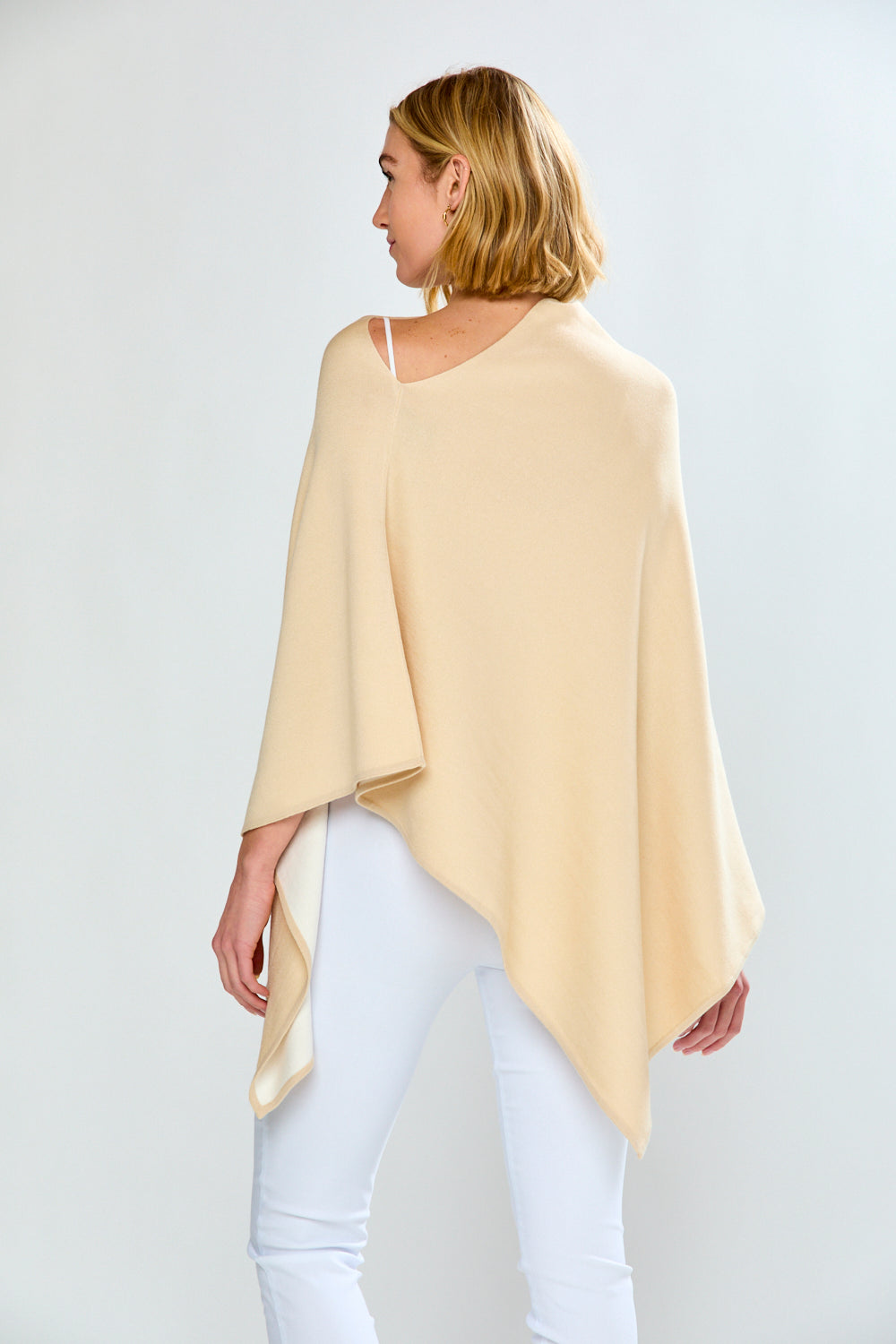 Woman wearing a light yellow poncho over a white top and pants on a plain background