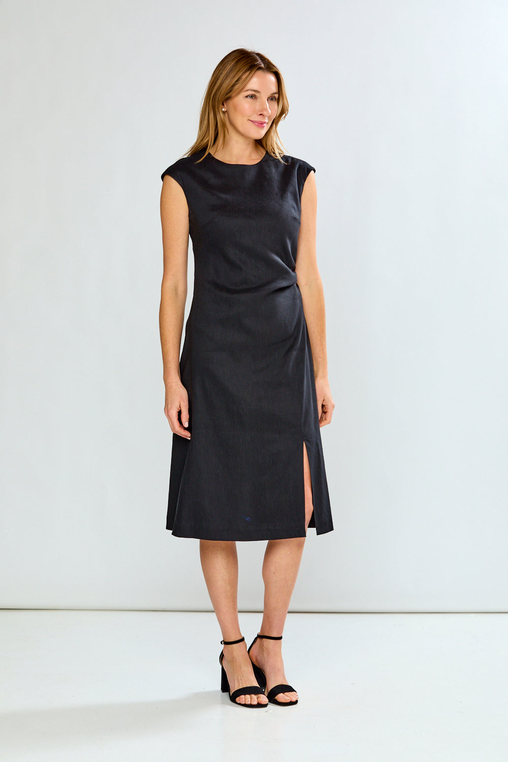 Woman wearing a black sleeveless dress with a slit on a white background