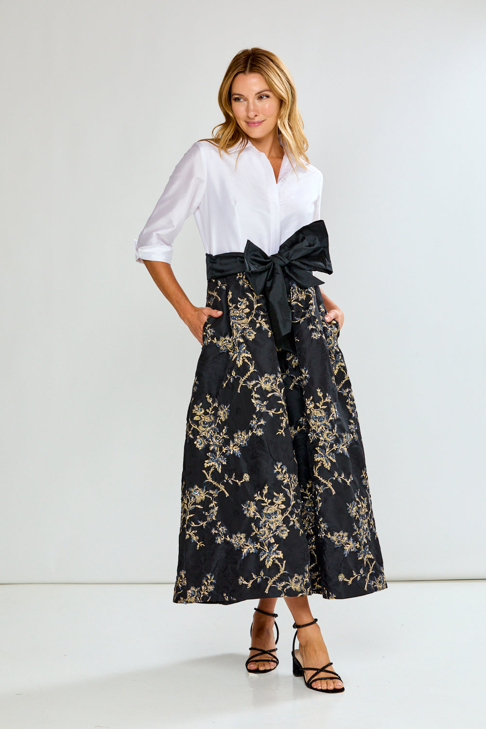 Woman wearing a dress with a white blouse and black floral skirt with a large bow on a white background