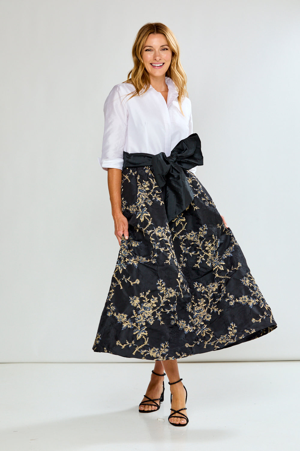 Woman wearing a dress with a white blouse and black floral skirt with a large bow on a white background
