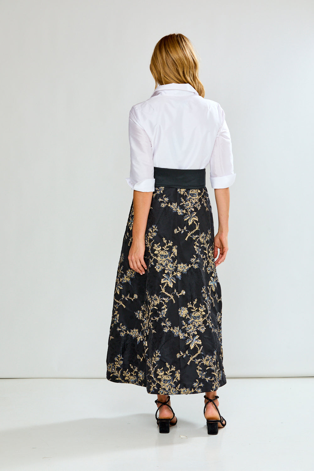 Woman wearing a dress with a white blouse and black floral skirt with a large bow on a white background
