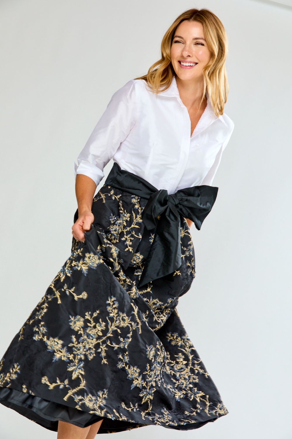 Woman wearing a dress with a white blouse and black floral skirt with a large bow on a white background