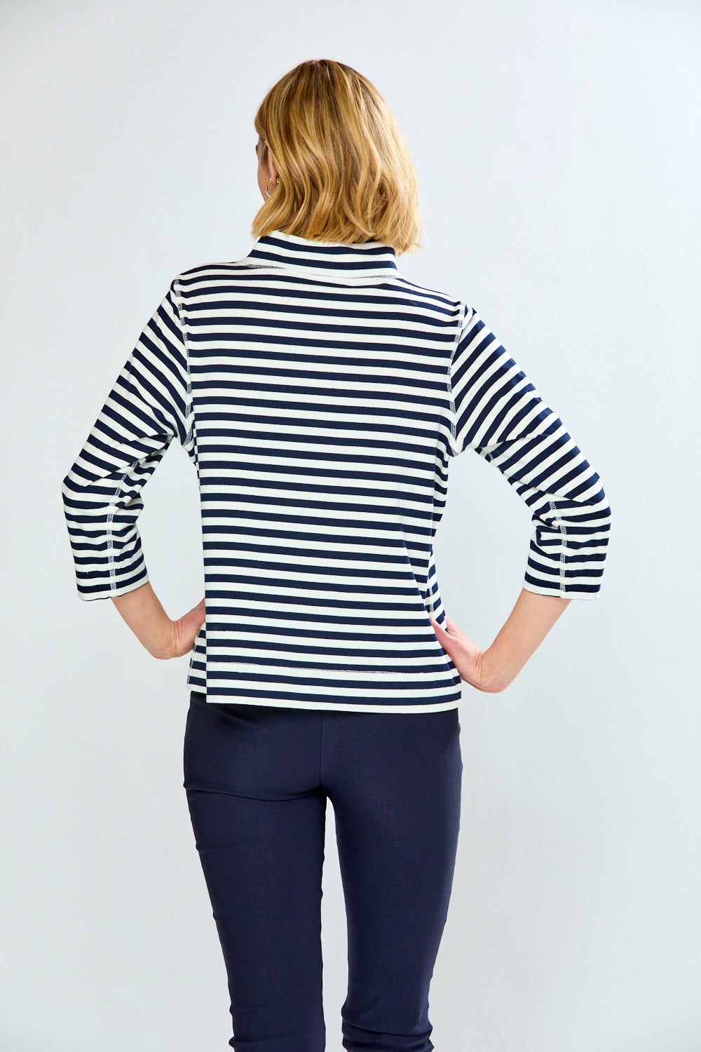 Woman wearing a black and white striped shirt with navy pants on a white background