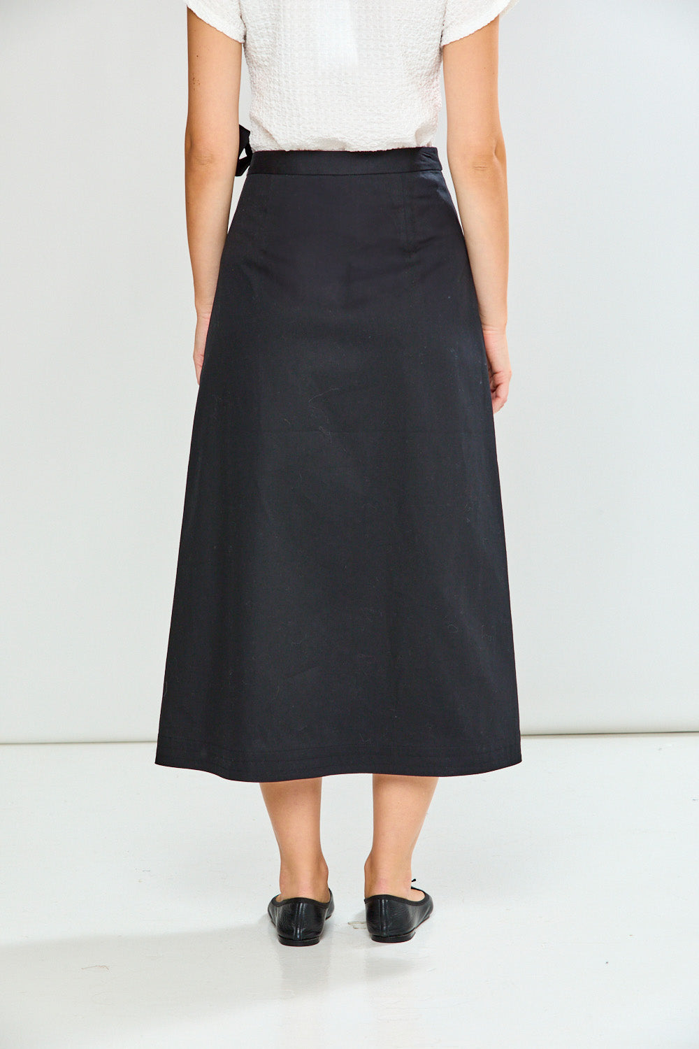 Person wearing a black skirt and white top on a plain background