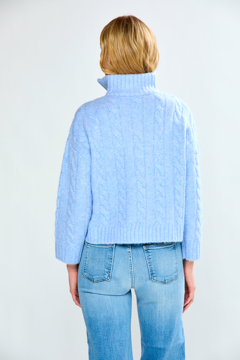 Woman wearing a denim cable knit sweater and blue jeans on a white background