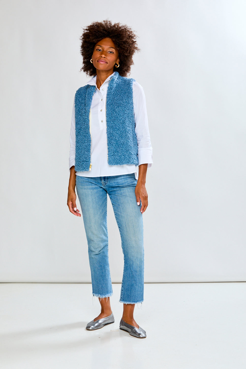 Woman wearing a blue textured vest over a white shirt and jeans on a white background