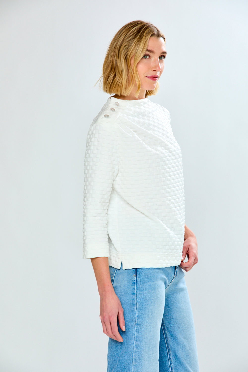 Woman wearing a white quilted jacket and light blue jeans on a white background