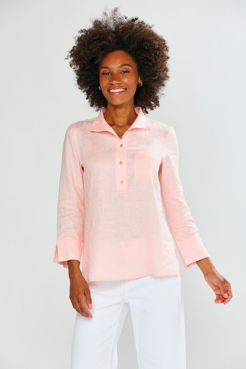 Woman wearing a light pink long-sleeve shirt and white pants on a plain background