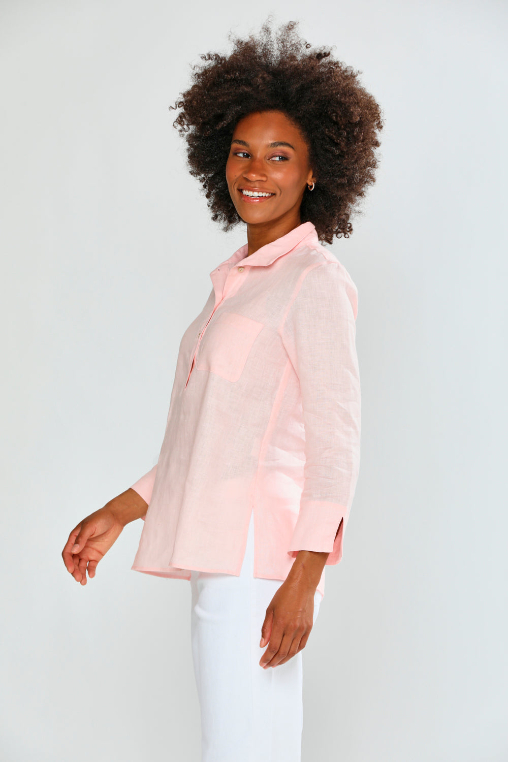 Woman wearing a light pink blouse and white pants against a plain background