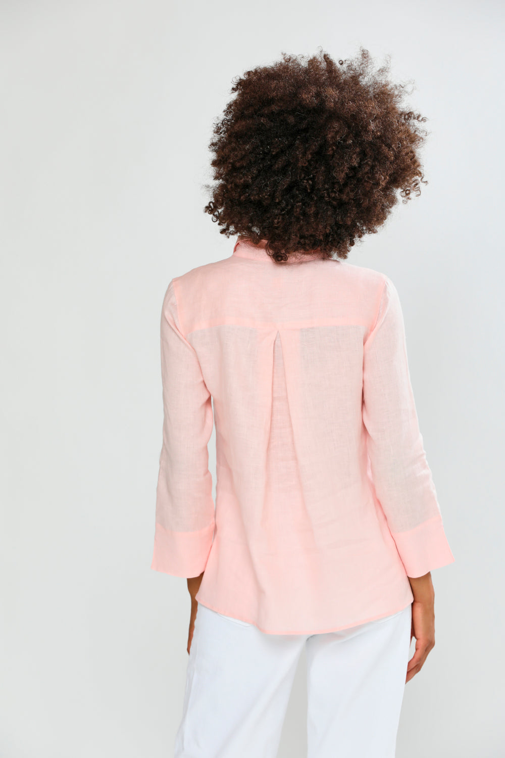 Person wearing a light pink blouse with a plain background