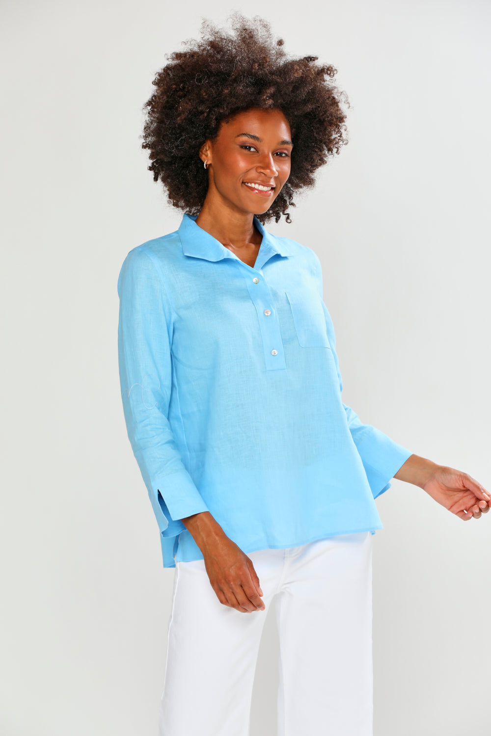 Woman wearing a light blue shirt and white pants on a plain background