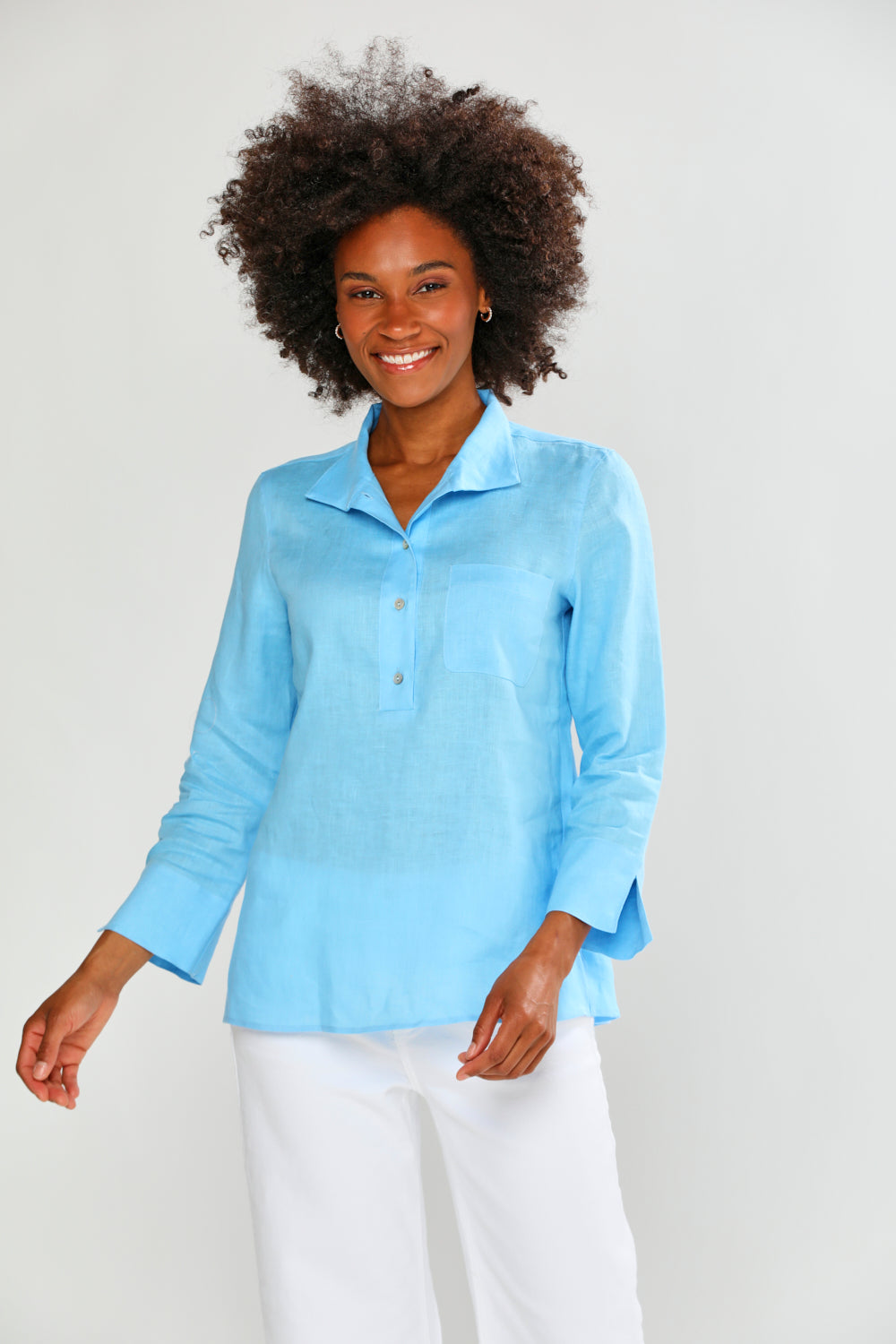 Woman wearing a light blue long-sleeve shirt and white pants on a plain background